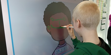 Powiększ grafikę: Chłopiec dorysowuje elementy twarzy postaci na tablicy multimedialnej.