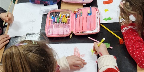 Powiększ grafikę: Uczniowie siedzą przy stole, rysują i kolorują bożonarodzeniowe symbole.