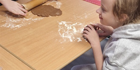 Powiększ grafikę: Chłopiec wałkuje ciasto na pierniki, dziewczynka i chłopiec przyglądają się.