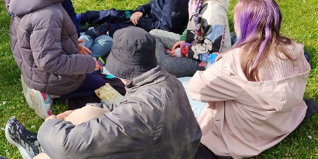 Powiększ grafikę: Pięcioro uczniów siedzi w kole na trawie.