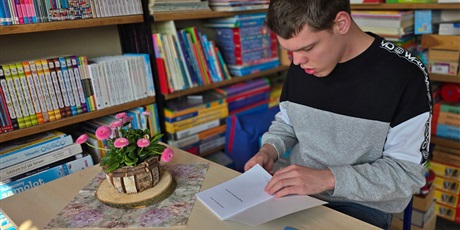 Powiększ grafikę: Przy stoliku w bibliotece siedzi chłopiec, ogląda książkę.