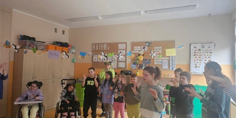 Powiększ grafikę: Uczniowie stoją w rzędach i naśladują gesty nauczyciela.