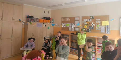 Powiększ grafikę: Uczniowie stoją w rzędach i naśladują gesty nauczyciela.