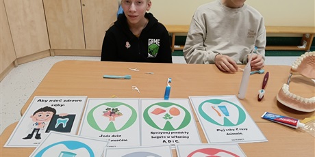 Powiększ grafikę: Chłopcy siedzą przy stoliku, na którym leżą obrazki z hasłami o higienie.