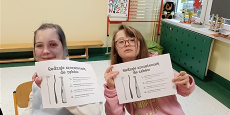 Powiększ grafikę: Dwie dziewczynki siedza przy stoliku, trzymają kartki, na których przedstawione są rodzaje szczoteczek do zębów.