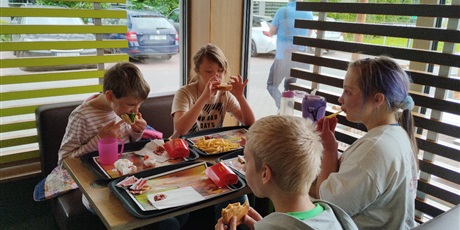 Powiększ grafikę: Trzy dziewczynki i chłopiec siedzą przy stoliku w McDonalds. Przed nimi tace z zamówieniami.