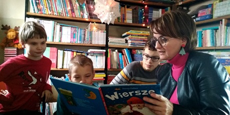 Powiększ grafikę: Trzech chłopców na tle regałów z książkami patrzy w książkę i słucha nauczyciela.