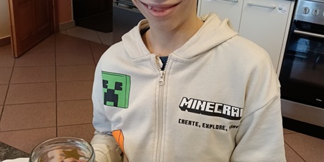 Powiększ grafikę: Chłopiec siedzi przy stole, trzyma ozdabiany słoik.