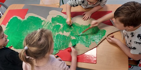 Powiększ grafikę: uczniowie malują zieloną farbą wyciętą z papieru choinkę