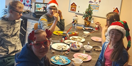 Powiększ grafikę: Uczniowie w świątecznych czapkach siedzą dookoła stołu, na którym rozłożone są kleje, brokaty i elementy świąteczne wycięte ze sklejki.