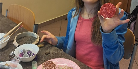 Powiększ grafikę: Dziewczynka pokazuje magnes w kształcie bombki ozdobiony brokatem.