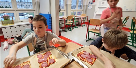 Powiększ grafikę: Chłopcy układają dodatki na spodach pizzy.