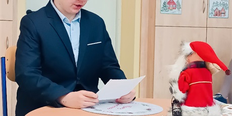 Powiększ grafikę: Chłopiec ubrany w marynarkę, siedzi przy stoliku i czyta.