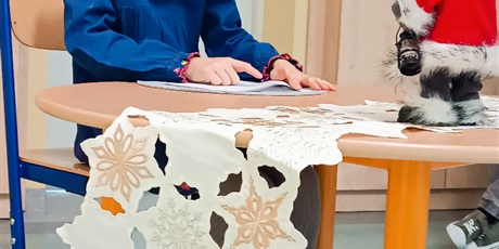 Powiększ grafikę: Dziewczynka siedzi przy stoliku, na którym stoi figurka Mikołaja i czyta.