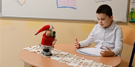 Powiększ grafikę: Chłopiec siedzi przy stoliku, na którym stoi figurkaMikołaja i czyta.