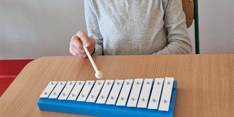 Powiększ grafikę: Chłopiec siedzi przy stoliku, gra na cymbałkach.