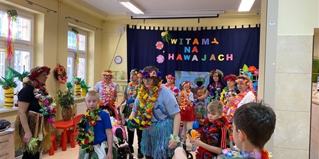 Powiększ grafikę: Uczniowie ubrani w stroje z hawajskimi elementami tańczą w sali z hawajskimi dekoracjami.