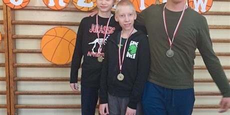 Powiększ grafikę: Trzech uczniów z medalami na szyi stoją na tle drabinek.