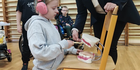 Powiększ grafikę: Dziewczynka w słuchawkach na uszach ćwiczy jak należy myć zęby.