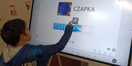 Powiększ grafikę: Chłopiec układa z liter nazwę przedmiotu na obrazku na tablicy multimedialnej.