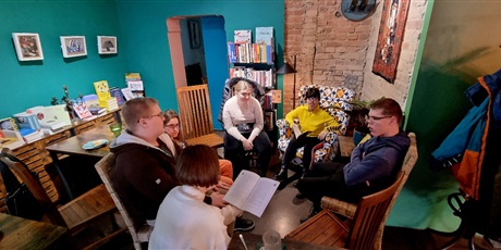 Powiększ grafikę: Sześcioro uczniów siedzi w kręgu w kawiarni słucha czytającego nauczyciela.