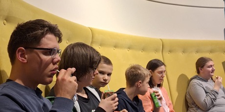 Powiększ grafikę: Uczniowie siedzą na żółtej kanapie, piją sok z kartonika.