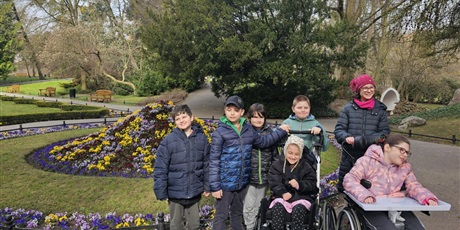 Powiększ grafikę: Grupa uczniów w parku na tle klombu z bratkami.