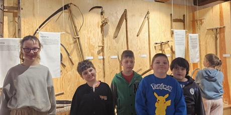 Powiększ grafikę: Uczniowie stoją grupą w sali muzeum na tle różnych rodzajów kos.