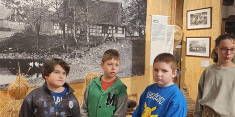 Powiększ grafikę: Uczniowie stoją grupą w sali muzeum na tle zdjęcia starej wsi.