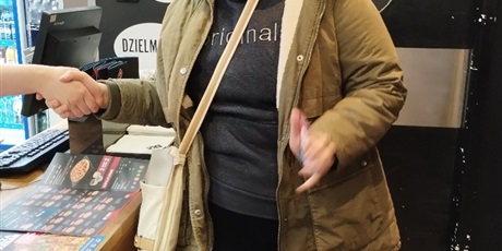 Powiększ grafikę: Dziewczynka stoi przy ladzie, podaje rękę sprzedawcy.