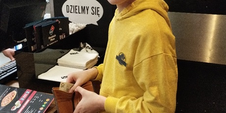 Powiększ grafikę: Chłopiec stoi przy ladzi, wyjmuje pieniądze z portfela.