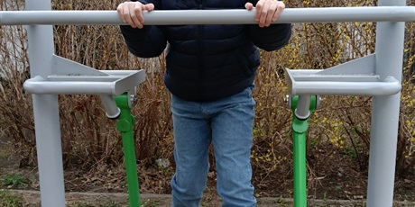 Powiększ grafikę: Uczeń korzysta z sprzętu na siłowni pod chmurką.