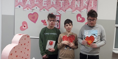 Powiększ grafikę: Trzech chłopców stoi na tle napisu "Walentynki", trzymają w rękach wykonane przez siebie kartki walentynkowe.