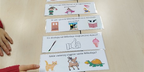 Powiększ grafikę: Na stoliku leżą zapisane pytania z graficznymi odpowiedziami do wyboru.