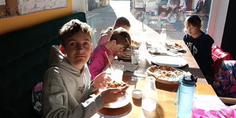 Powiększ grafikę: Uczniowie siedzą przy stoliku w pizzerii, na którym stoją pizze.