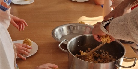 Powiększ grafikę: Uczniowie wyjmują z garnka masę ryżową i lepią z niej kulki. 