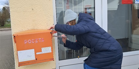 Powiększ grafikę: Dziewczynka wrzuca list do skrzynki wiszącej na budynku.
