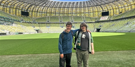 Powiększ grafikę: Uczniowie stoją na tle stadionu.