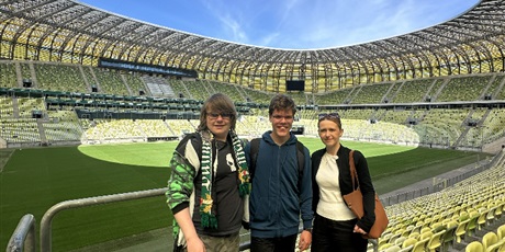 Powiększ grafikę: Uczniowie z nauczycielką stoją na tle dstadionu widzianego z góry.
