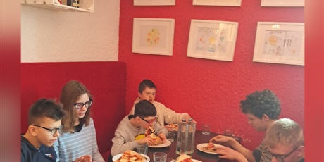 Powiększ grafikę: Uczniowie jedzą pizzę w pizzerii.