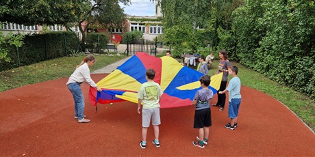 Powiększ grafikę: Uczniowie trzymaja dookoła chustę animacyjną i podnoszą ją do góry.