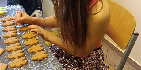 Powiększ grafikę: Dziewczynka siedziprzy stole i ozdabia pierniki.