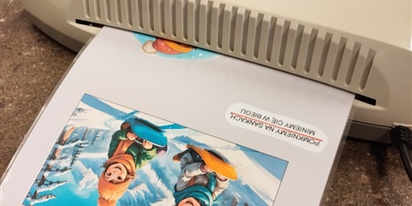 Powiększ grafikę: Kartka z zimowym obrazkiem wychodzi z laminarki.