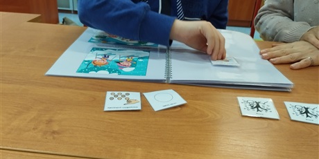 Powiększ grafikę: Chłopiec przyczepia w książce etykietkę z symbolem PCS.