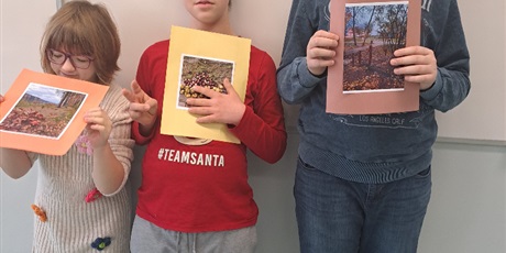 Powiększ grafikę: Uczennica i dwóch uczniów stoją przy tablicy. Uczniowie trzymają w rękach swoje konkursowe prace. 