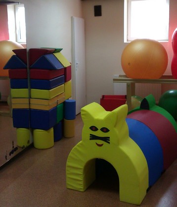 Sala rehabilitacyjna z wyposażona w duże piłki, kolorowe poduchy i tunel.