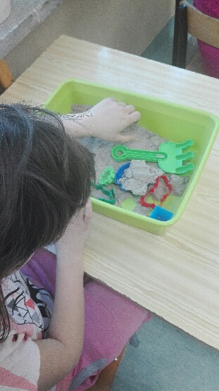 Dziecko, które bawi się piaskiem sensorycznym za pomocą foremek o różnym kształcie.